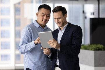 Asian and Hispanic men teammates reviewing documents or reports, looking at presentations or...