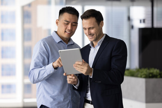 Asian and Hispanic men teammates reviewing documents or reports, looking at presentations or slideshows, analyzing data and information relevant to joint project using digital tablet. Teamwork, tech