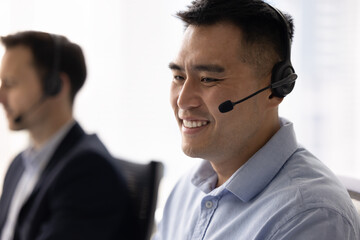 Close up of smiling Chinese man, call center, customer services employee wear headset provides FAQ...