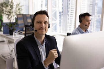Middle-aged 40s Hispanic man, call center employee equipped with headsets sitting in modern...