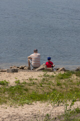 Father and son fishing on the riverbank. Family fishing. Single father. Father's Day. Back to the camera. Outdoor recreation. Family bonding. Shared leisure. Rear view. Adults and children.