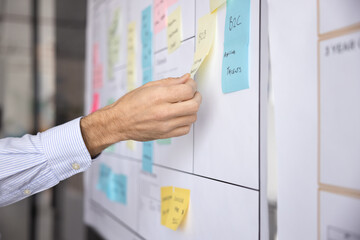 Project manager attaching or removing sticky notes as reminders on whiteboard, leaves message for team, writes deadlines, corporate goals or individual tasks, close up shot. Planning, brainstorming