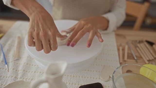 Young woman potter shapes slab of clay with bare hands on pottery wheel in studio; craft creativity patience.
