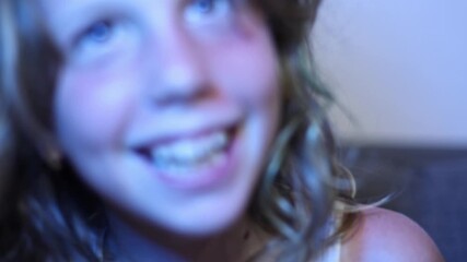 A playful girl with light brown hair transitions from blur to focus, grinning mischievously and shaking her head before fading back into a soft blur, capturing a fleeting moment of childhood joy