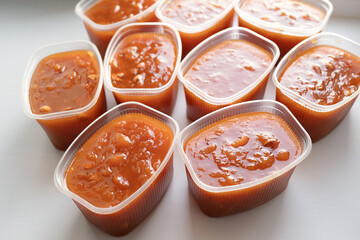 Fresh homemade apricot preserve in several transparent plastic containers arranged on a white...