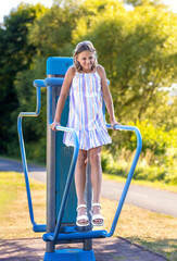 Young girl exercising on outdoor exercise machines. Woman exercising outdoors in the city park. Healthy lifestyle on city playground