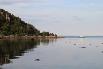 Summer landscape with a boat in a bay. Travel and a view on a riverside with horizon. Charlevoix landscape. Water reflection in a bay and coastline.