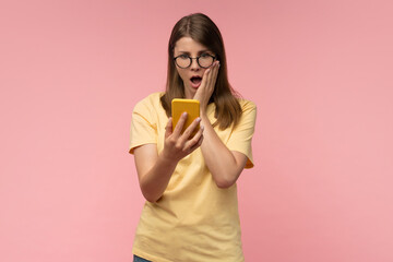 Shocked young woman in trendy glasses looking at smartphone with amazed face, surprised by betting...