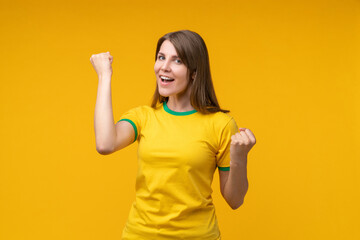 Joyful smiling young woman in yellow t-shirt cheering  making winners gesture yes with both fists...