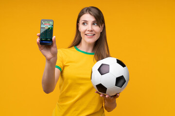 Happy young woman holding soccer ball and smartphone with betting app on screen
