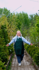 Portrait of happy female gardener standing among bright greenery of her garden