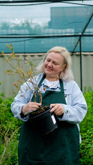Portrait of happy female gardener standing among bright greenery of her garden