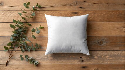 A simple white rectangular pillow rests on a rustic wooden surface adorned with delicate green eucalyptus leaves