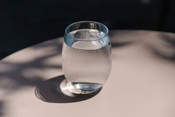 Minimal luxury aesthetic concept. Bohemian crystal glass with sparkling sunlight shadow on the grey beige background	