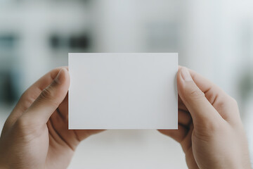 A hand holding a blank white card against a blurred background. Great for message insertion or design placement for promotional purposes.