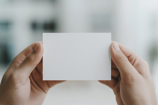A hand holding a blank white card against a blurred background. Great for message insertion or design placement for promotional purposes.