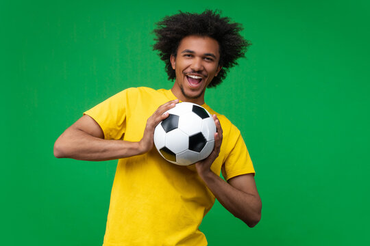Happy young African man with afro hairstyle laughing joyfully while holding a soccer ball