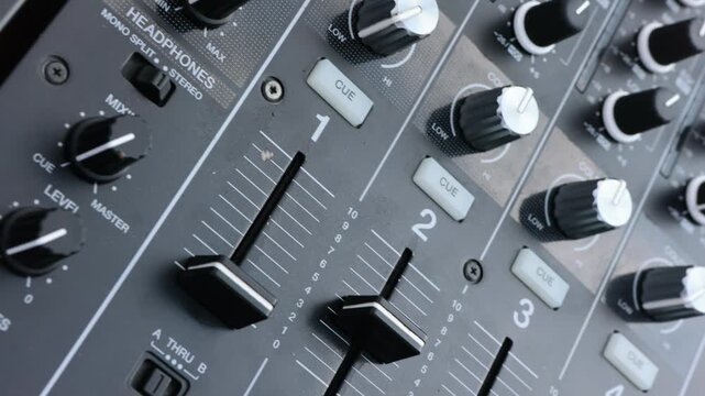 Close-up of a professional audio mixer's faders and knobs,