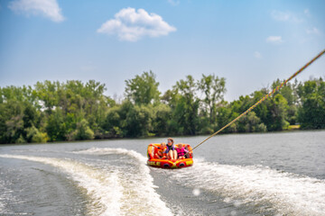 mother and children in an Inflatable raft being pulled at a high speed by a boat in a recreational activity called tubing