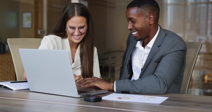 Happy diverse business man and woman working on online product at laptop together, typing, discussing Internet marketing report, sales growth, ideas for e-commerce project development