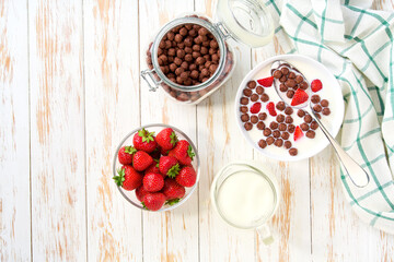 Healthy breakfast with chocolate corn balls and strawberry on a white wooden table, top view.