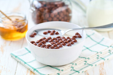chocolate corn balls in a bowl with milk and honey on a white wooden table.