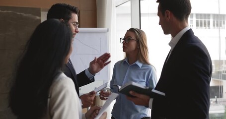 Four happy successful young diverse business colleagues talking in office boardroom, standing together, brainstorming, discussing creative ideas for teamwork, networking - Powered by Adobe