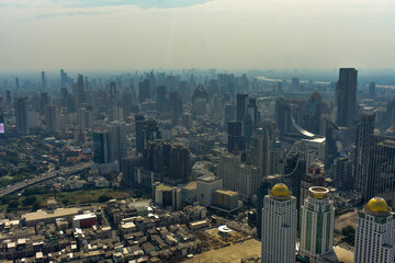 Panoramic urban skyline of Bangkok with numerous skyscrapers and buildings under a hazy sky.