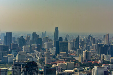 Panoramic urban skyline of Bangkok with numerous skyscrapers and buildings under a hazy sky.