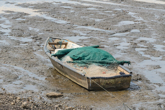Small fishing boat grounded in muddy shore with fishing nets