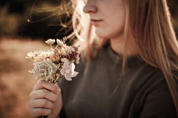 Young woman holding a bouquet of wildflowers in warm sunset light, close-up view of hands and face...