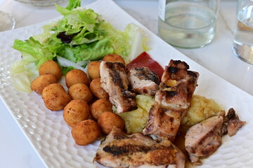 Plato de pollo asado en trozos con croquetas, ensalada de lechuga, puré de patatas y pimiento rojo