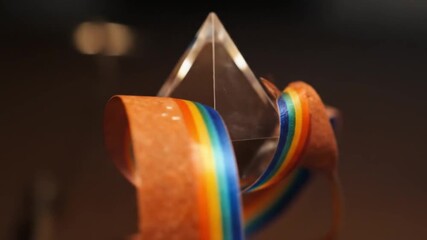 A clear prism with a rainbow ribbon wrapped around it on a dark background in a studio setting - Powered by Adobe