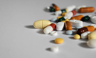 Assorted medical pills and capsules arranged on a white surface, with negative space on the left.
