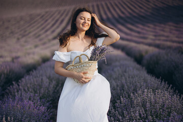Woman wearing white dress holding wicker basket enjoying lavender field