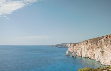 The rugged, white cliffs meet the sparkling turquoise Ionian sea near Zakynthos, Greece under a...