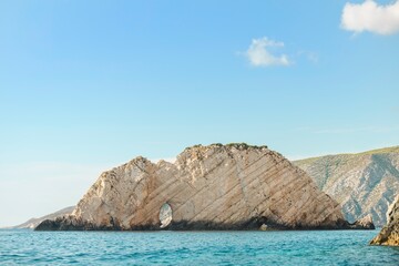 Fototapeta premium A rock island formation with a unique natural arch, set against the azure Aegean Sea and sky, creates a picturesque view in Greece