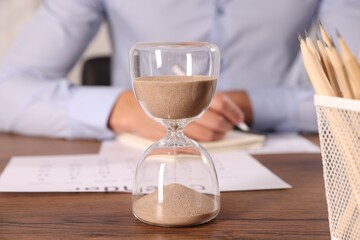 Deadline. Hourglass and man working at wooden table, selective focus