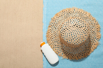 Beach towel, straw hat and sunscreen product on sand outdoors, flat lay. Space for text