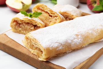Tasty apple strudels with powdered sugar and mint on white table, closeup