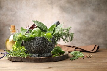 Mortar with different fresh herbs and peppercorns on wooden table against grey background, closeup
