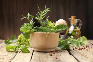 Mortar with different fresh herbs and peppercorns on wooden table against brown background, closeup
