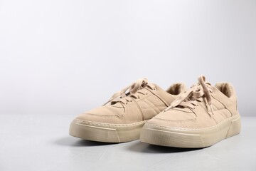 Pair of beige sneakers on light grey surface, closeup. Space for text