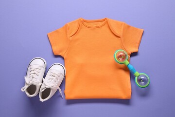 Bright baby onesie, accessory and shoes on violet background, flat lay