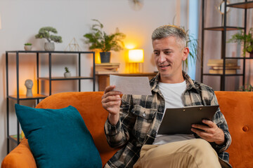 Man reading paper documents, working at home room. Freelance young guy businessman reviewing...