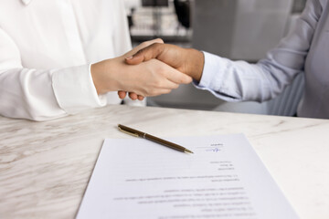 Close up shot of two women shaking hands seated at table with signed contract, establish...