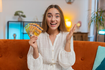 Successful rich Caucasian woman holding waving euro bill money fan sitting on couch at home room....