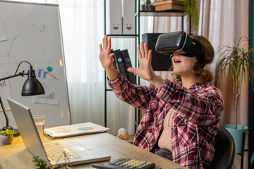 Young businesswoman using virtual reality futuristic technology VR app headset to simulation 3D 360 video at modern home office workplace. Excited manager freelancer. Remote distant online working.
