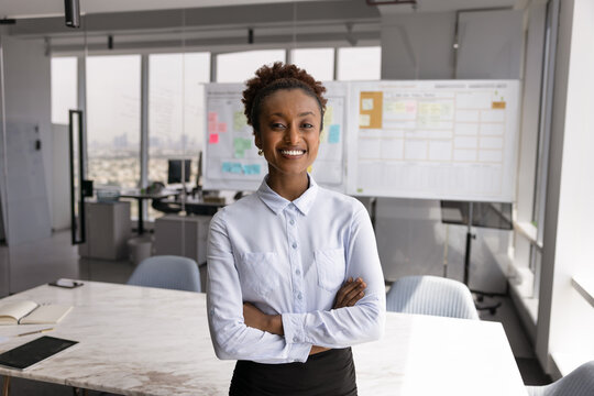 Empowered women in business, independence, professional success. Portrait of young attractive African businesswoman dressed in white shirt posing in conference room look at camera with contented smile - Powered by Adobe