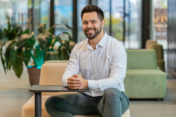 Portrait of happy smiling bearded businessman looking at camera and smiling in modern office lobby....